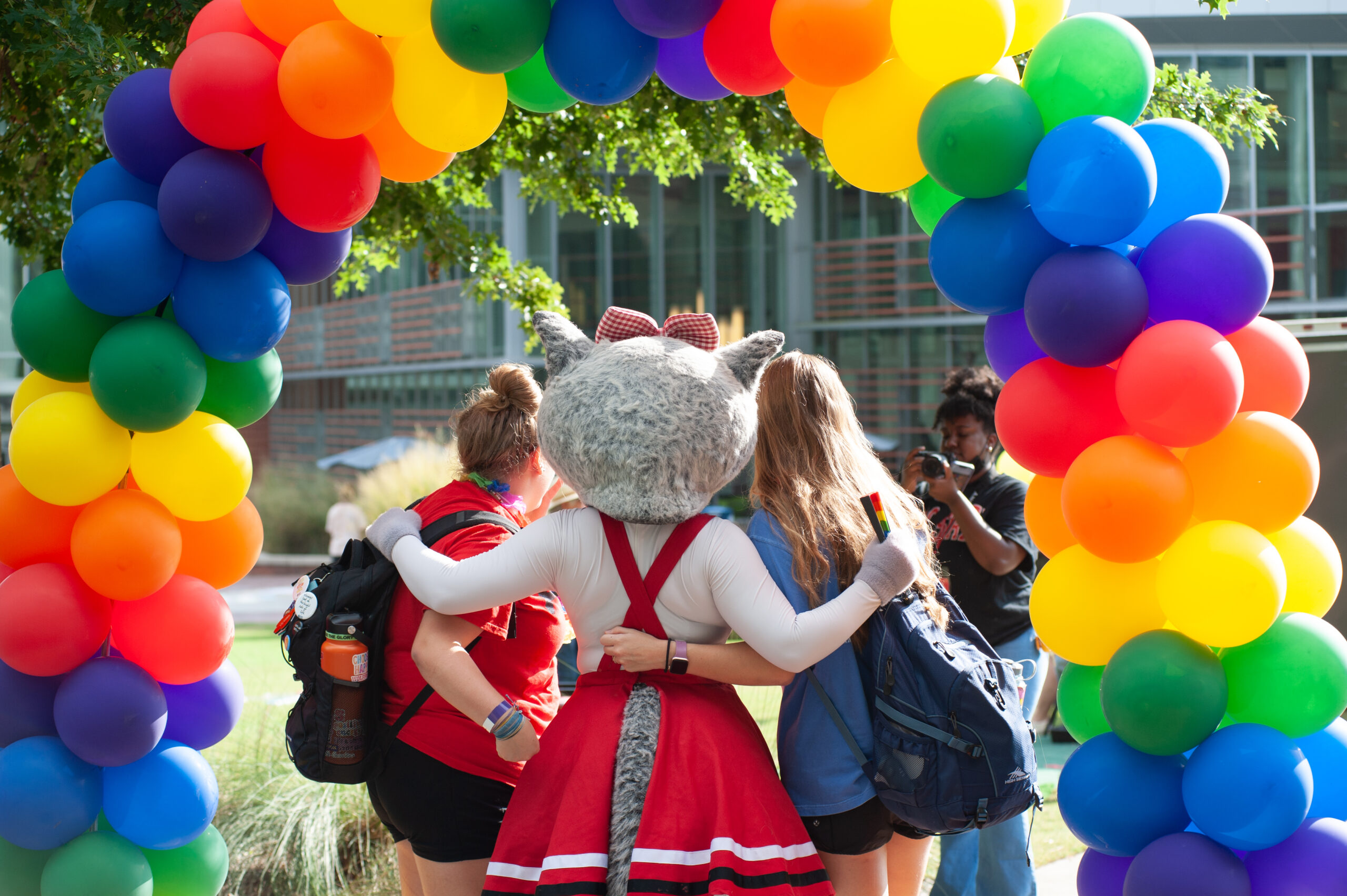 Back view of Mrs. Wolf and two students under multi-color balloon arch