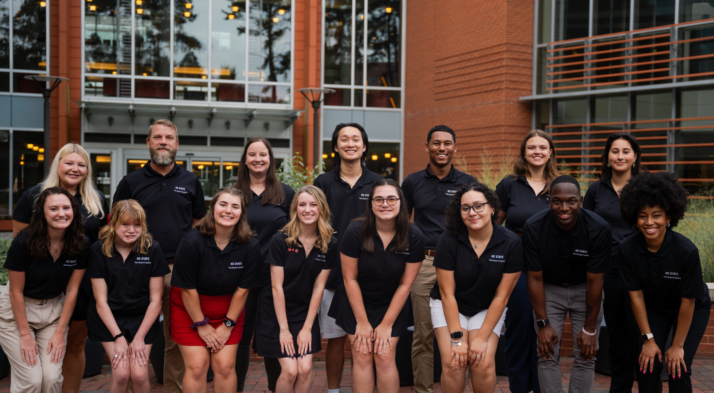 Group photo of a work team in black polos standing outside of a brick building